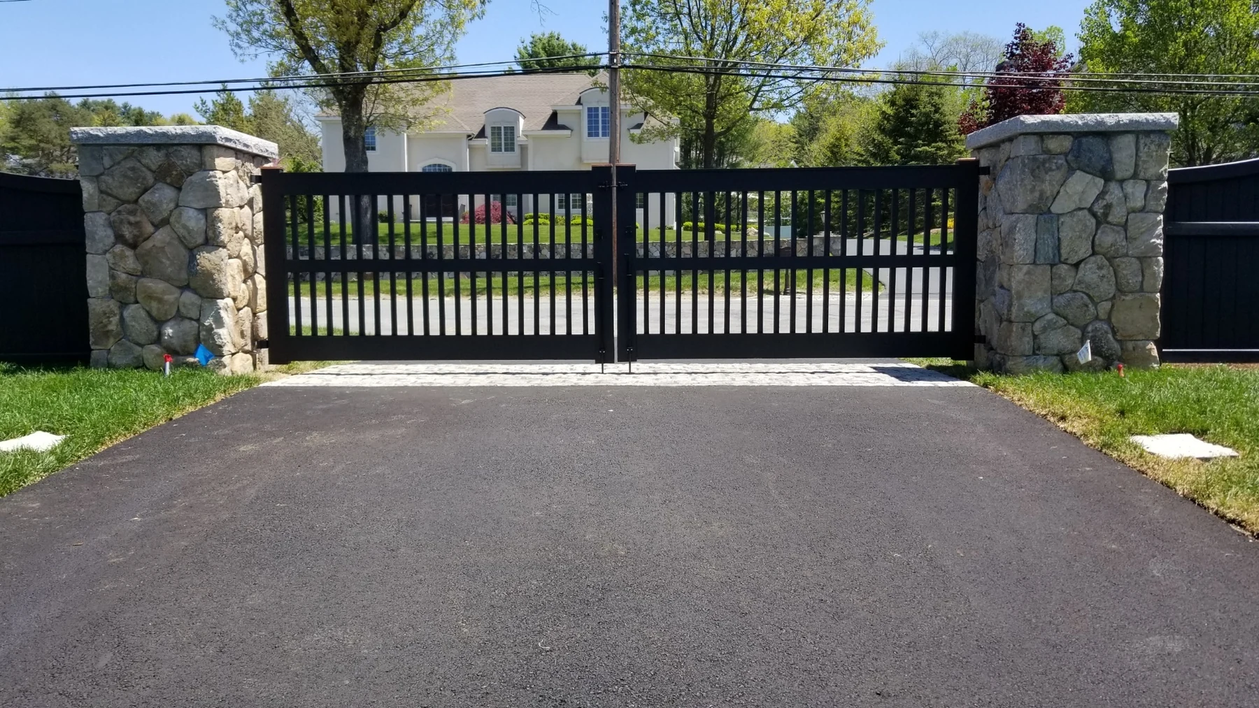 Black driveway gate and stone pillars installed by Milestone Fence